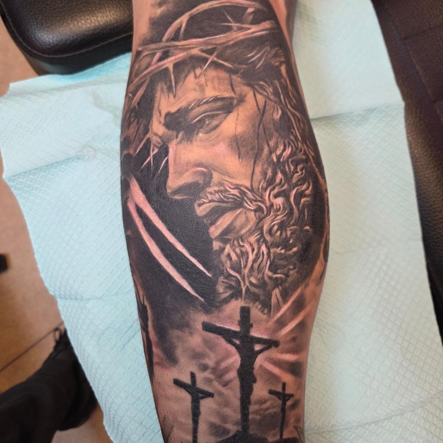 Black and grey Jesus with crown of thorns and crosses leg tattoo