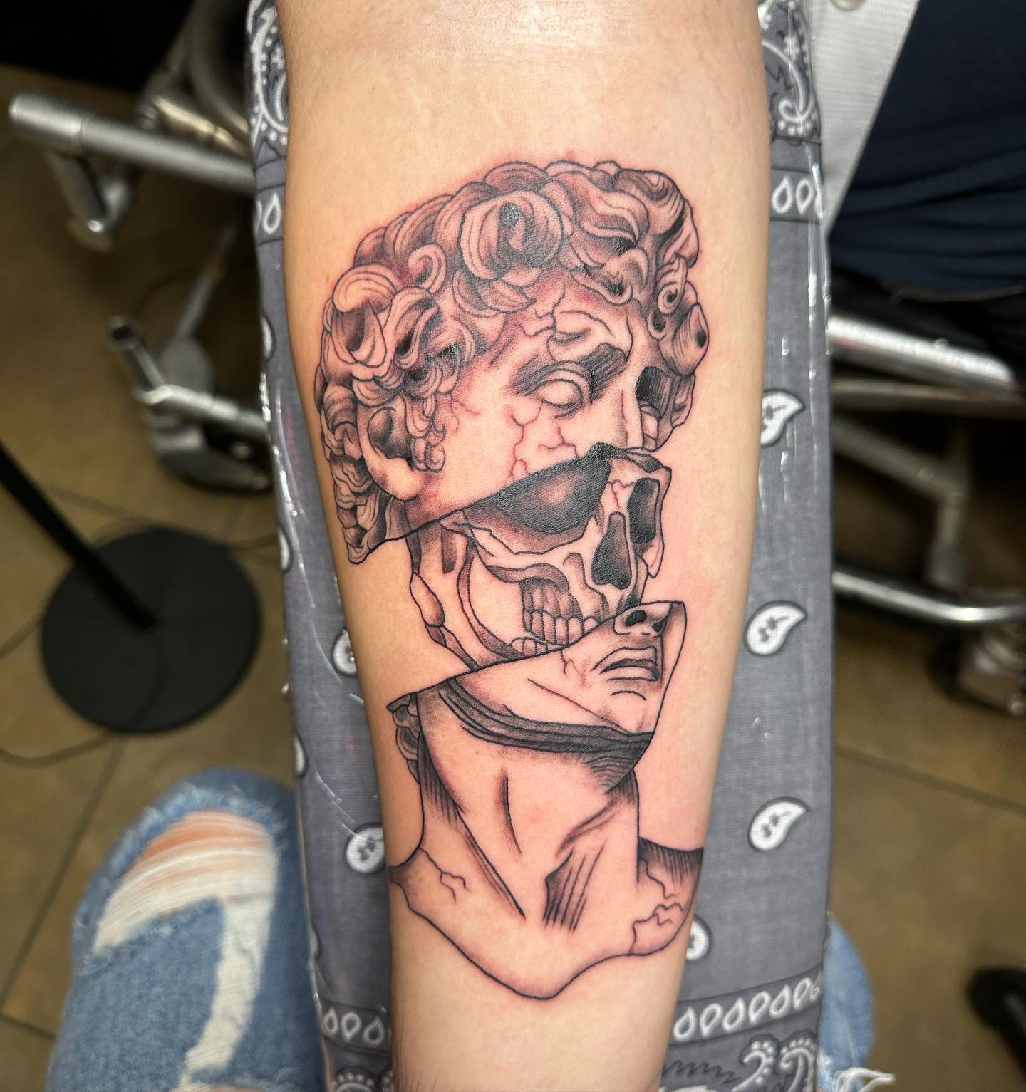 Black and grey fractured classical bust with skull tattoo on forearm