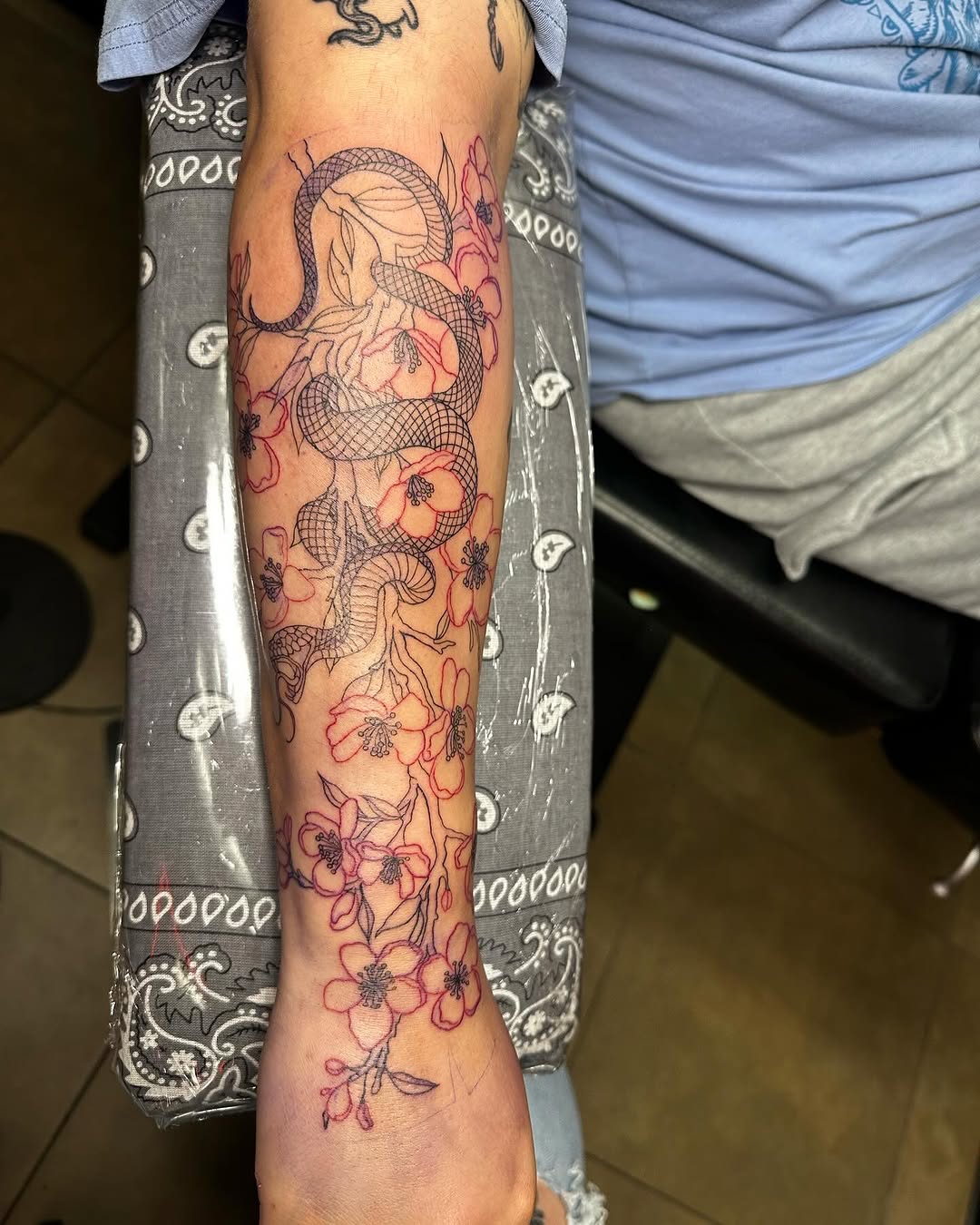 Fine line snake with cherry blossoms tattoo on forearm