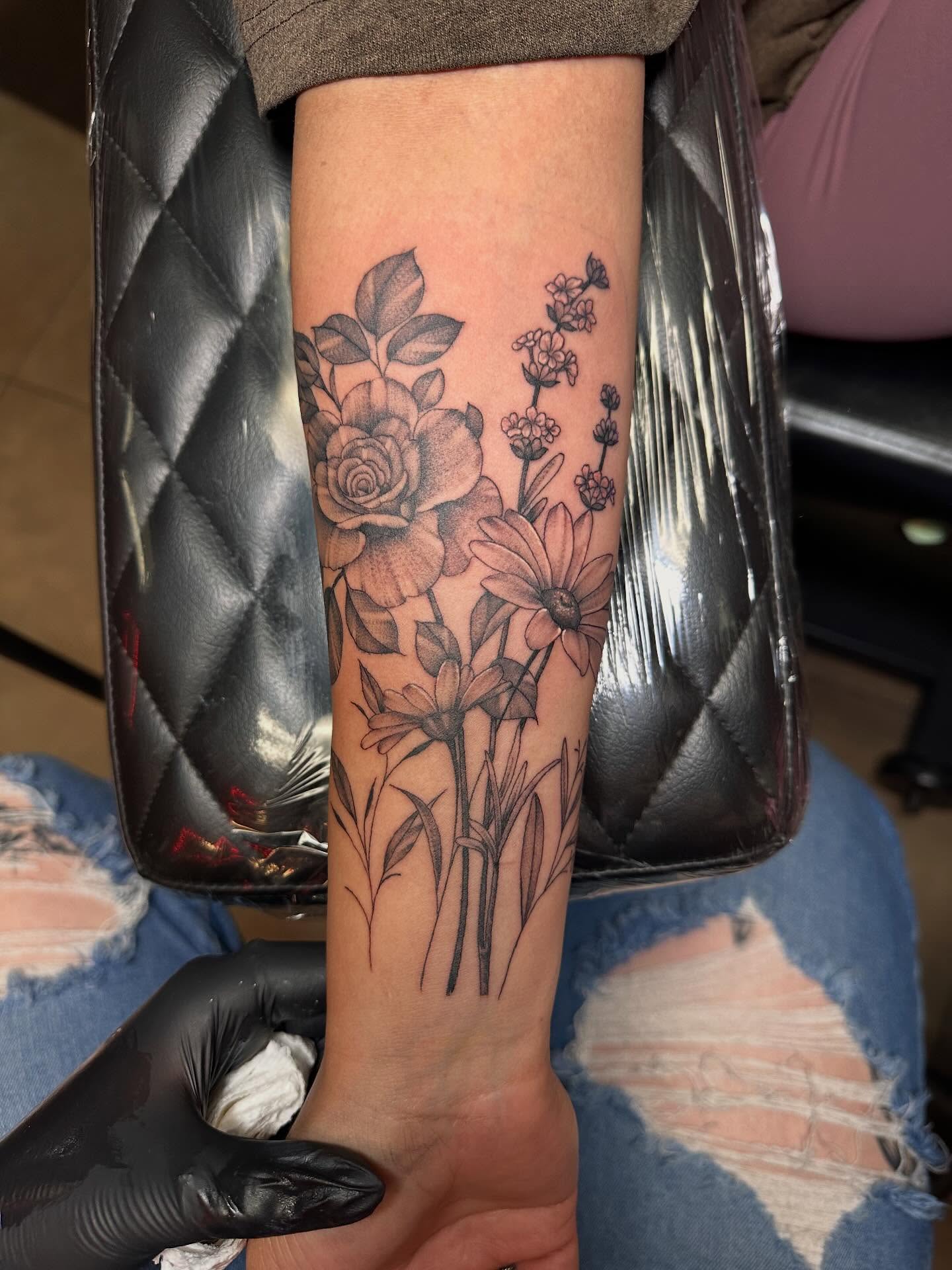 Black and grey floral forearm tattoo with rose, daisies, and lavender
