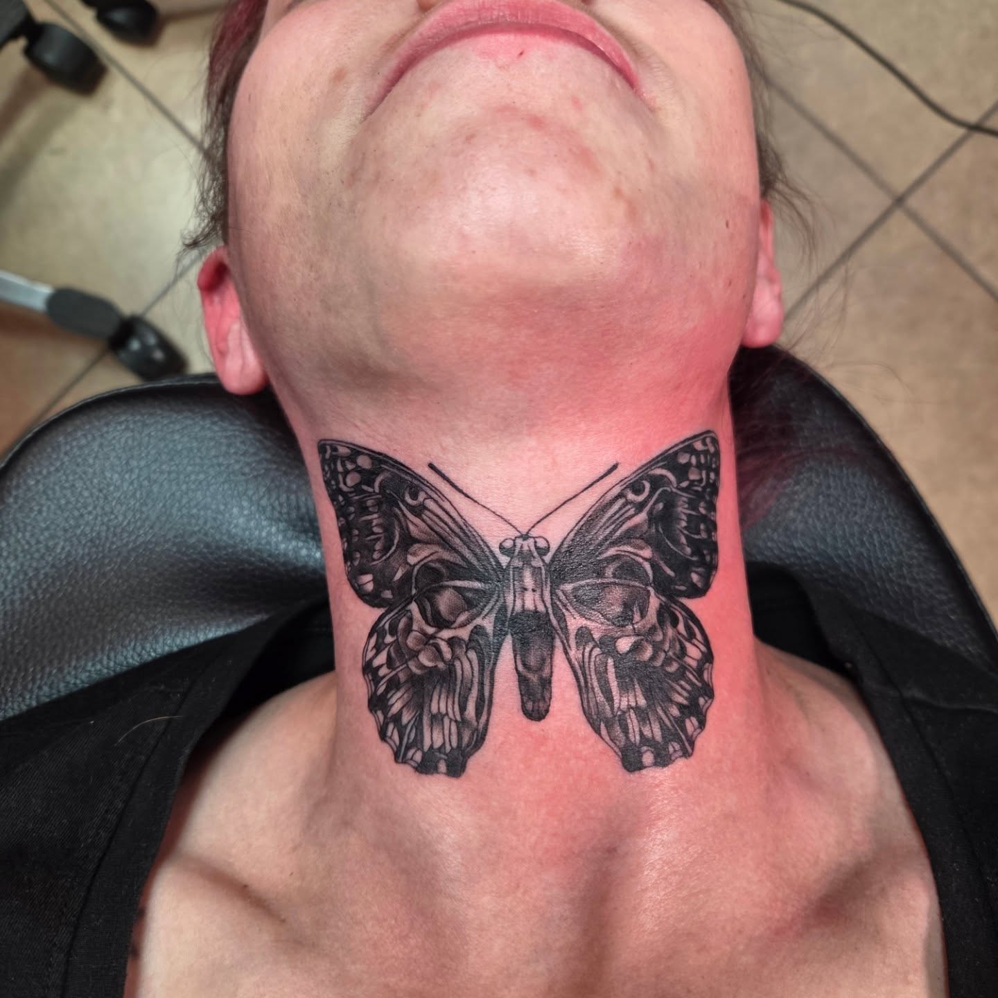 Black and grey skull-wing butterfly neck tattoo