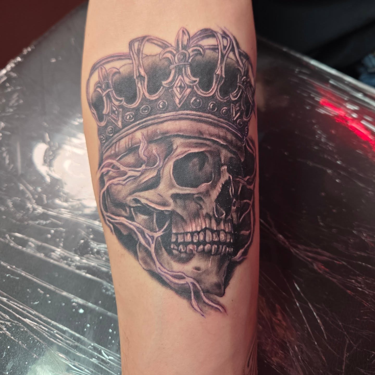 Black and grey crowned skull forearm tattoo
