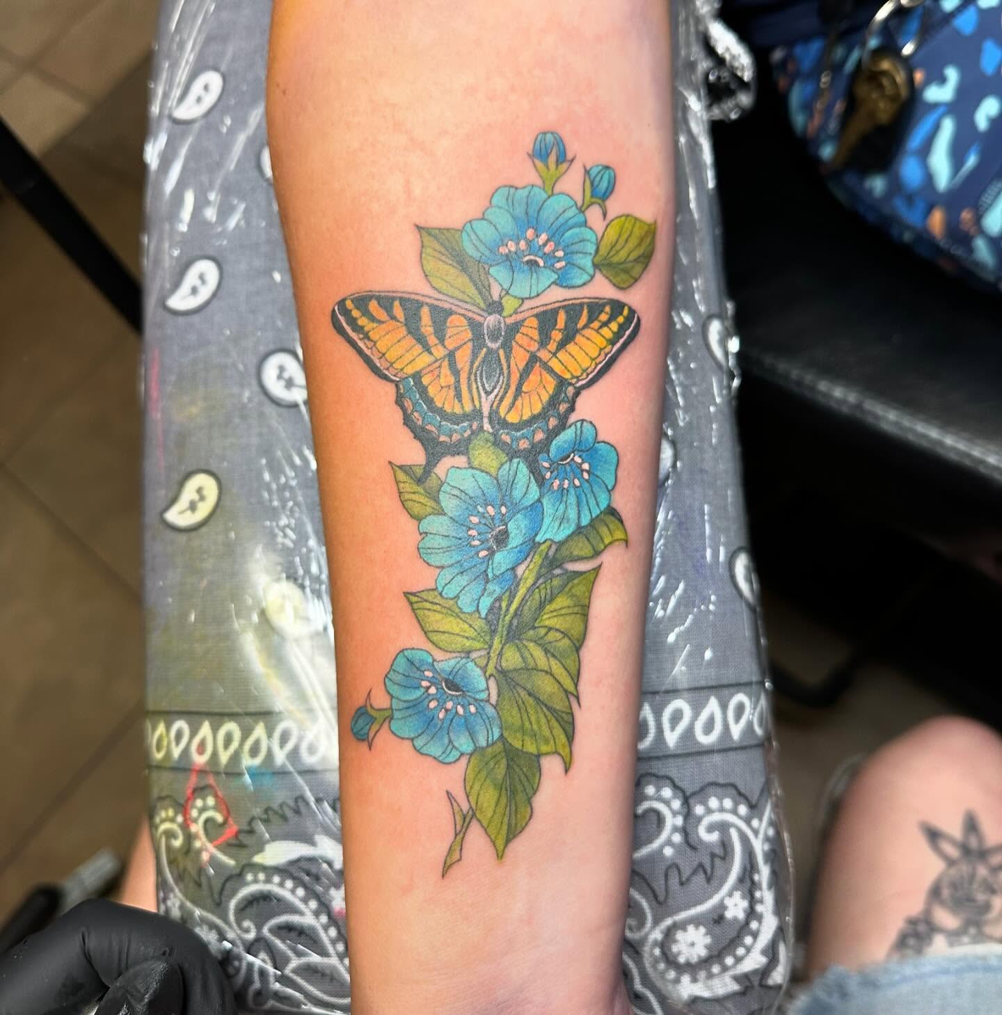 Color butterfly and blue wildflowers tattoo on forearm